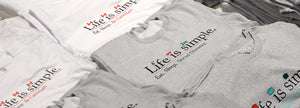 Flat lay of folded t-shirts reading "Life is simple. Eat. Sleep. Social Distance.